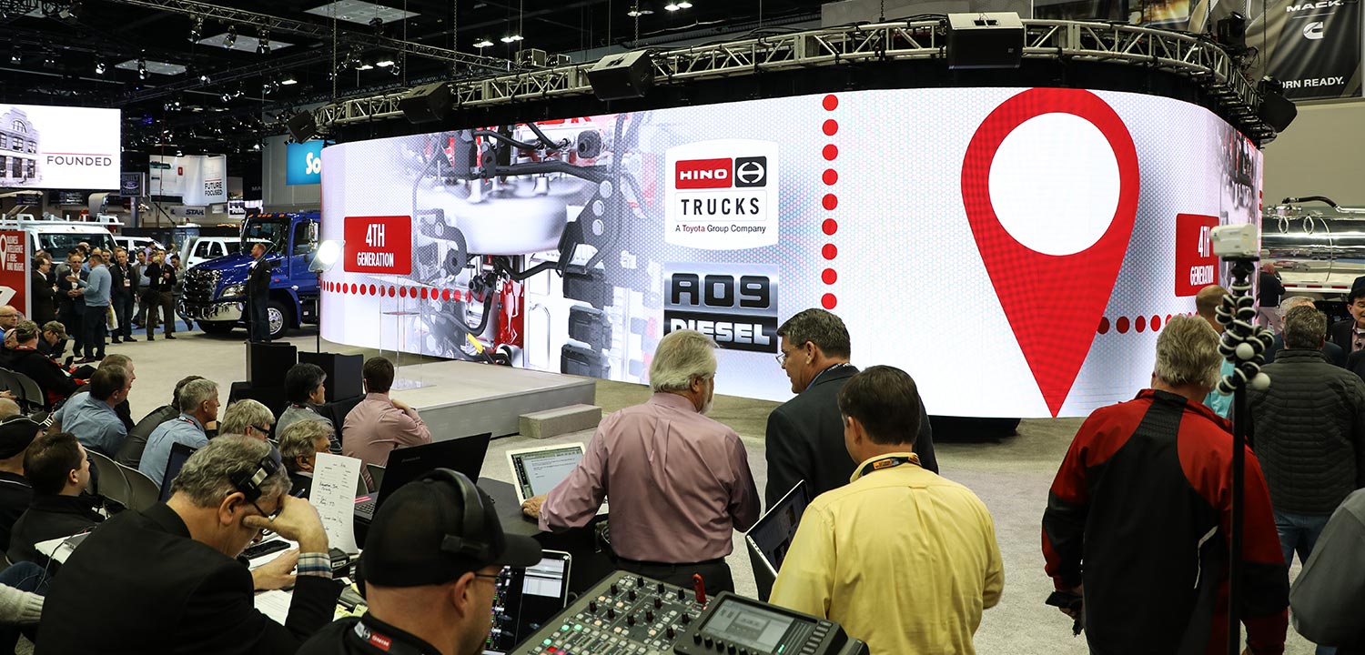Trade show presentation featuring LED video wall displaying Hino truck information with seated audience