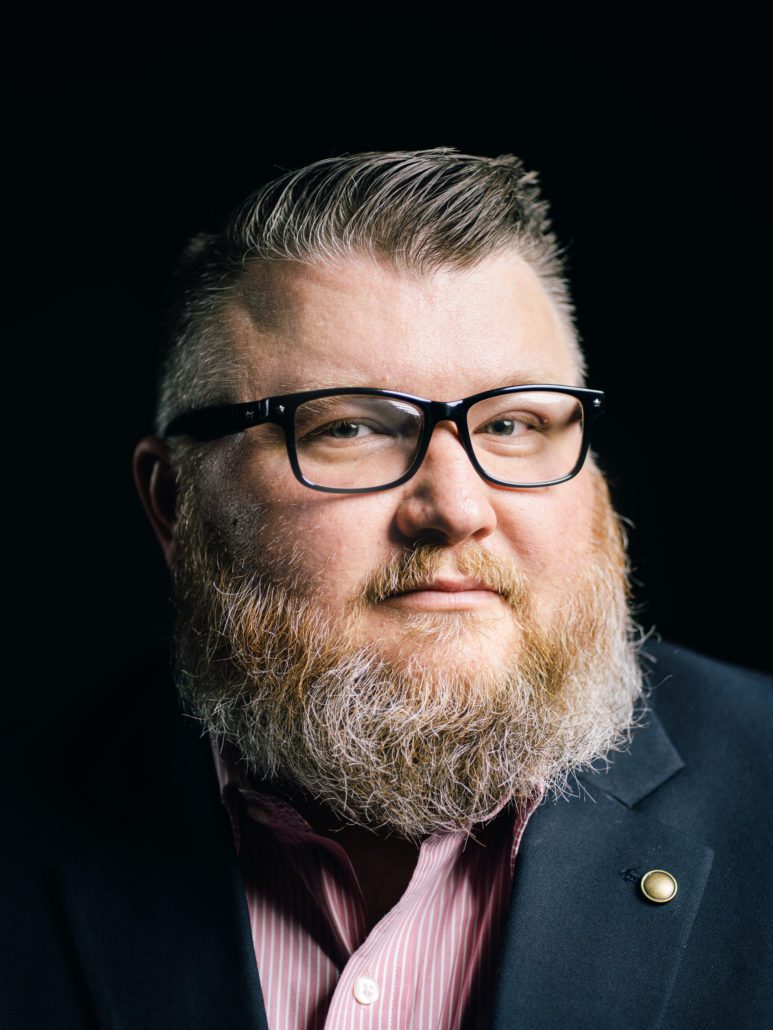 Man with glasses and beard wearing a suit.