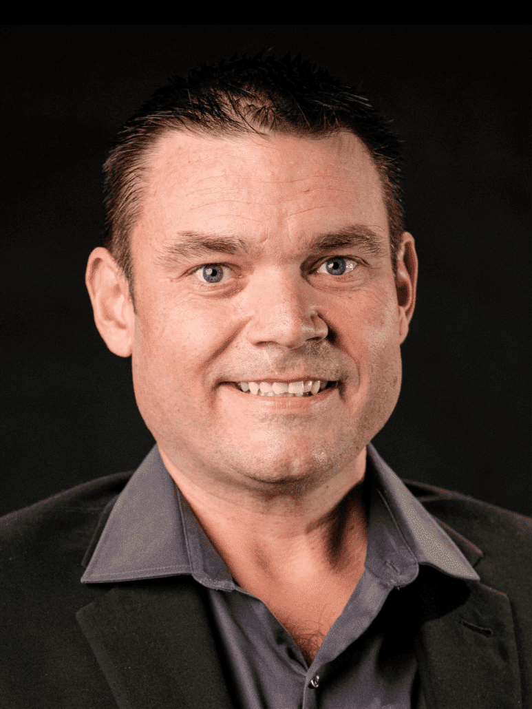 A person in a suit smiling against a dark background.