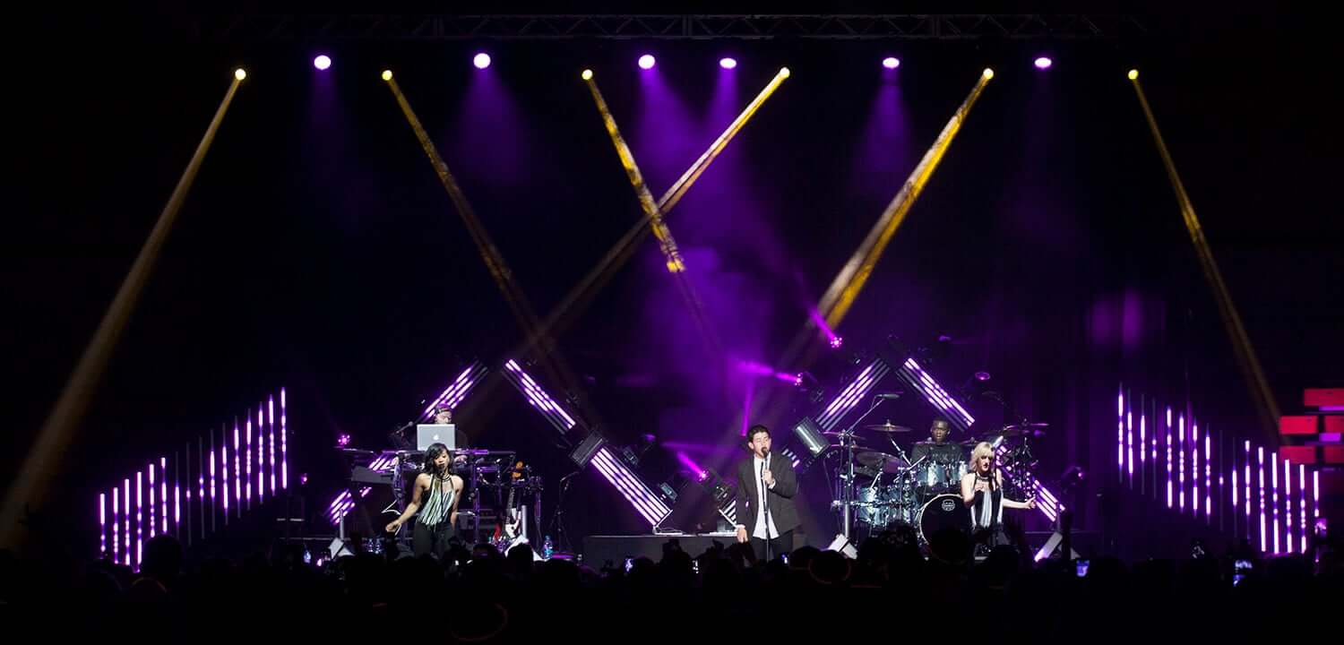 Professional rock band performing on stage with purple lighting and LED video displays