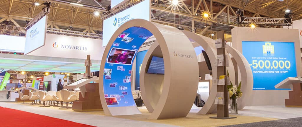 Novartis exhibition booth with digital screens and seating area.