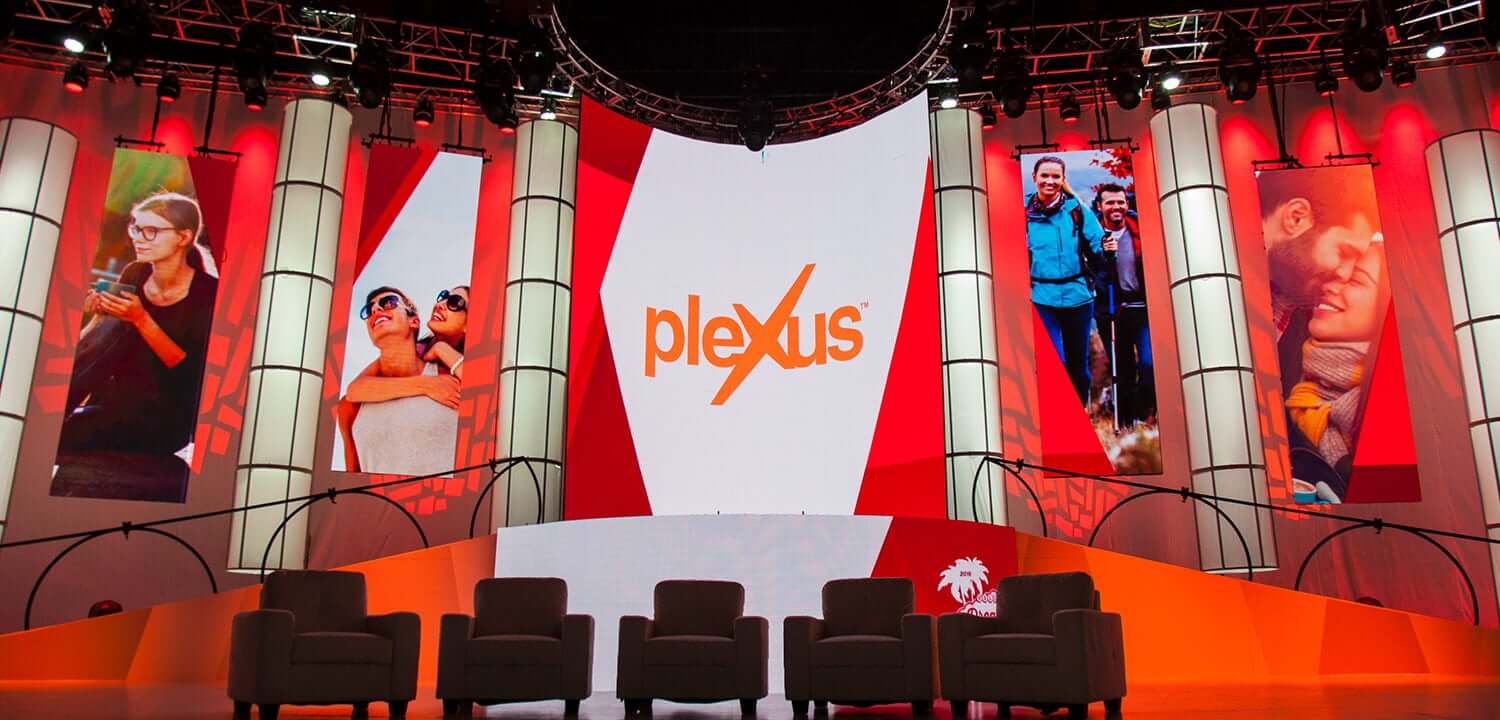Plexus corporate event with LED video walls displaying lifestyle imagery and red stage lighting