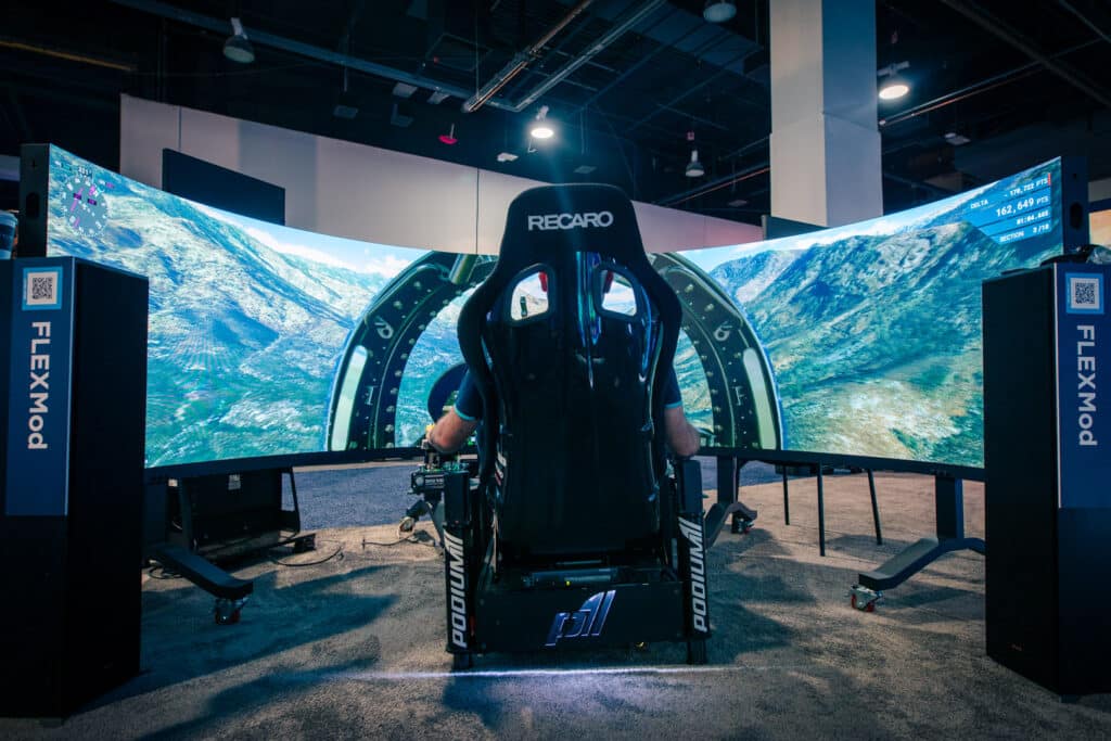 Person using flight simulator in curved screen setup at a tech expo.
