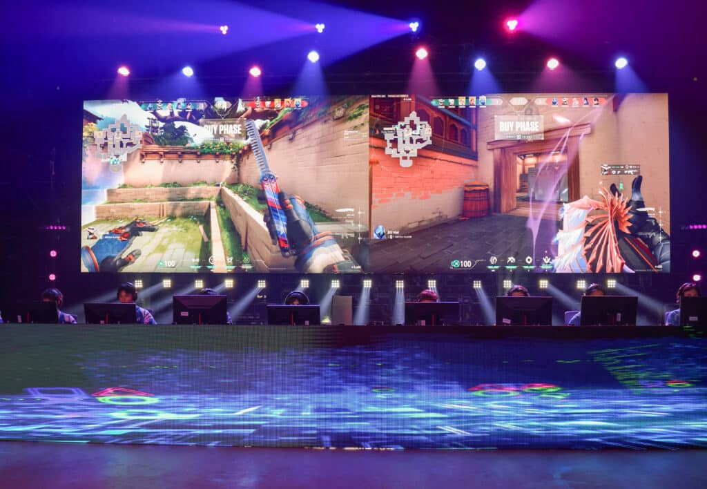Gamers competing in an esports tournament with Valorant on screen.