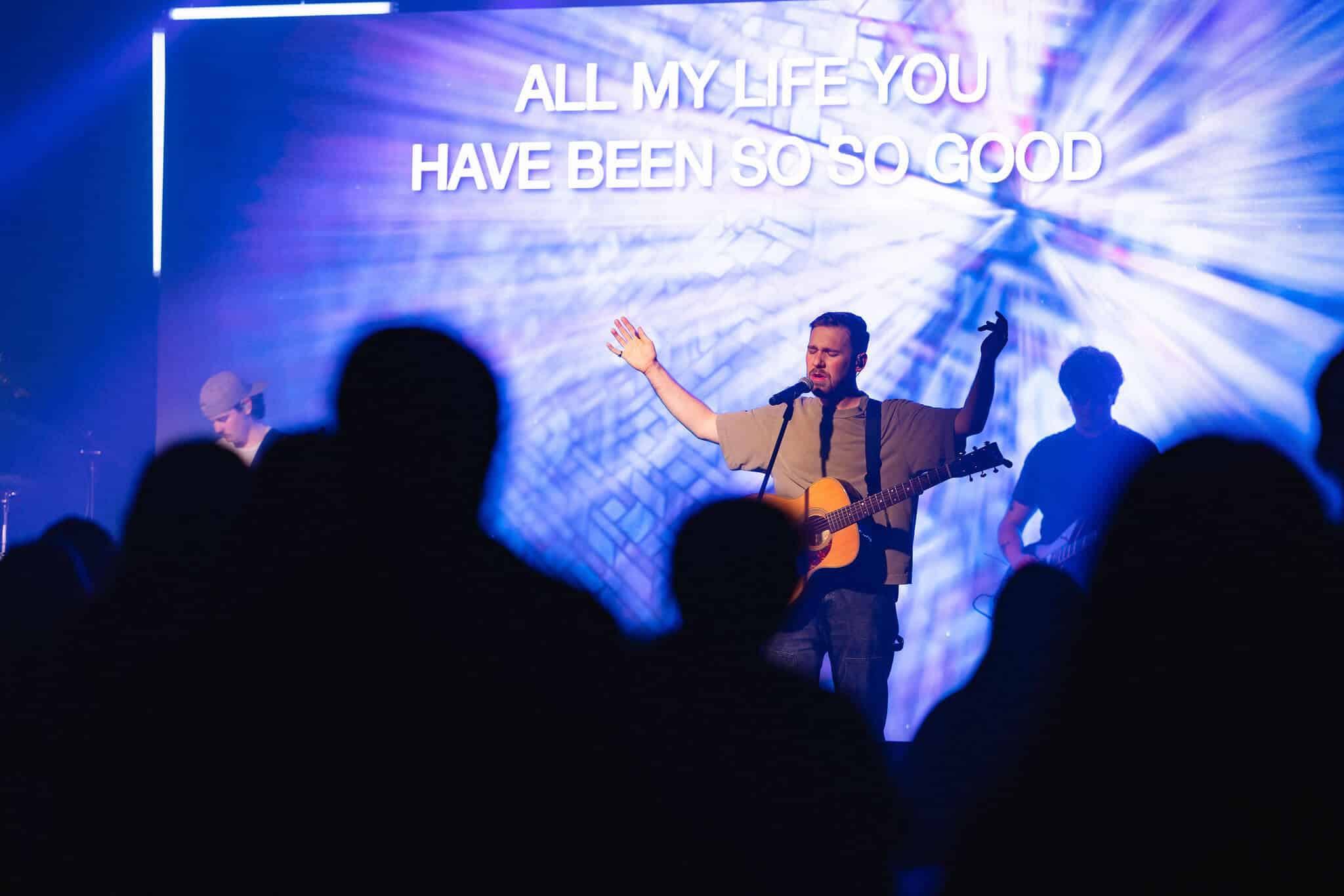 Live worship event with guitarist performing under bright stage lighting and LED backdrop