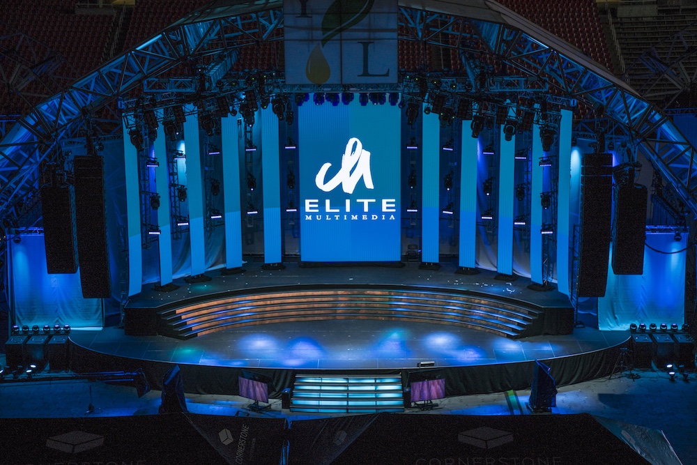 Arena stage washed in blue event lighting design, with curved LED video wall centered for a keynote