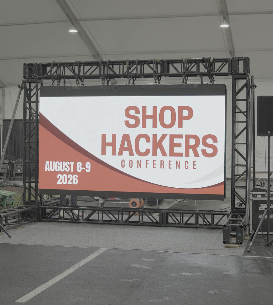 Large LED screen displaying Shop Hackers Conference branding mounted on truss framework